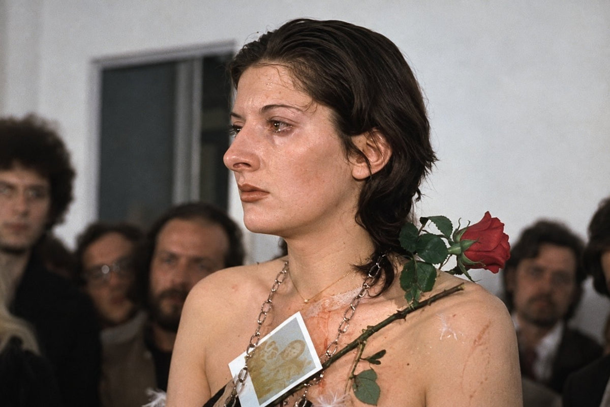 Colour editorial recreation: a woman with a red rose across her shoulder stands in front of a watching crowd